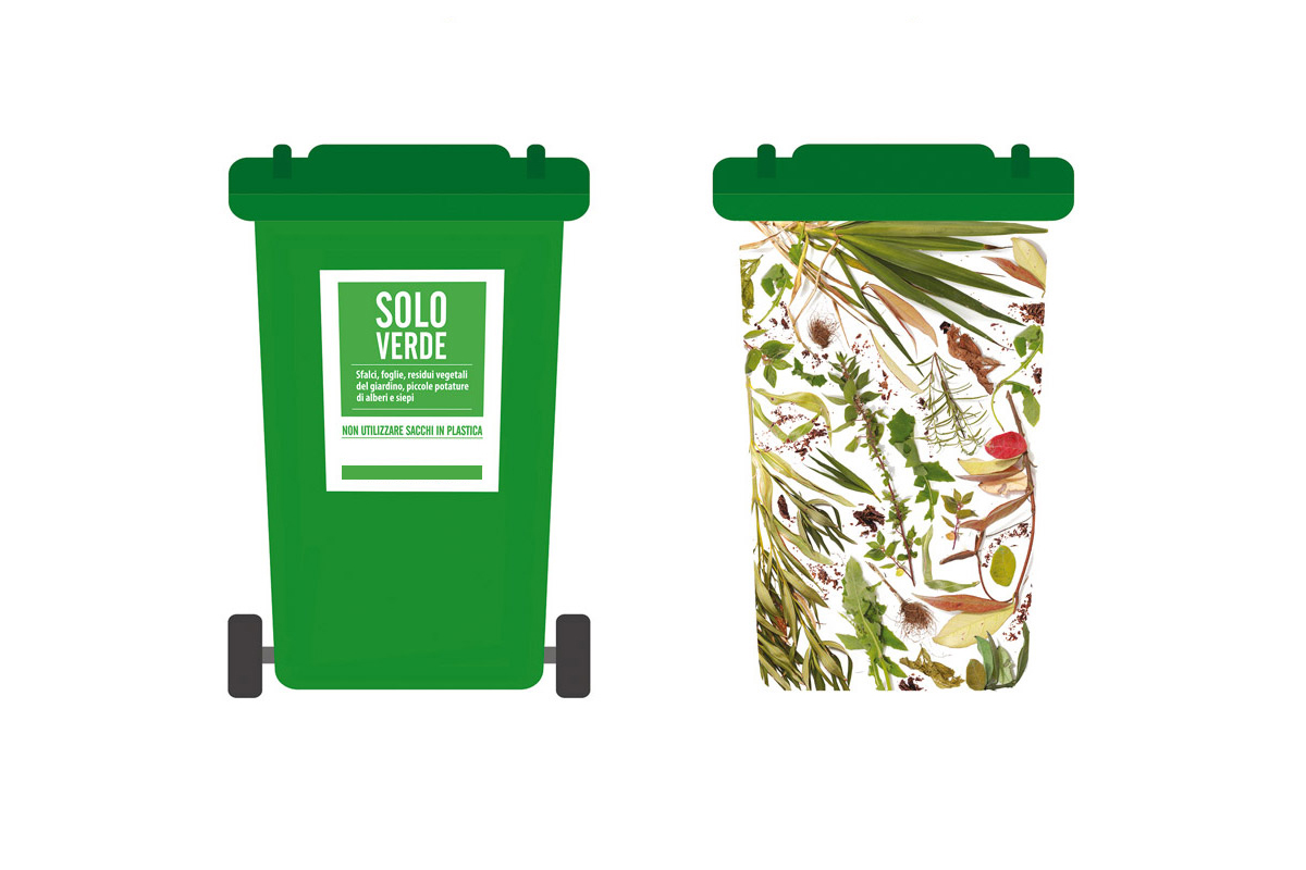 L’immagine mostra due bidoni verdi per la raccolta del verde.
Il bidone a sinistra è semplice, di colore verde uniforme, con un’etichetta bianca e verde che riporta la scritta “SOLO VERDE – Sfali, foglie, residui vegetali del giardino, piccole potature di alberi e siepi. Non utilizzare sacchi in plastica”. È un classico contenitore con coperchio e due ruote nere.

Il bidone a destra ha la stessa forma, ma l’intera superficie del contenitore è decorata con un motivo a sfondo bianco che raffigura foglie, rami, erbe e altri residui vegetali realistici. Il coperchio rimane verde uniforme, mentre il corpo del bidone sembra ricoperto da una stampa fotografica di materiale organico.
