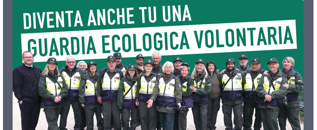 Banner promozionale con sfondo verde e grande scritta bianca in alto: “DIVENTA ANCHE TU UNA GUARDIA ECOLOGICA VOLONTARIA”.

In primo piano è raffigurato un gruppo numeroso di persone (circa 18), uomini e donne di età diverse, per lo più adulti e anziani, disposti in fila e sorridenti. Indossano uniformi coordinate composte da cappellino verde, giacca verde scuro e gilet ad alta visibilità giallo con bande riflettenti e stemmi identificativi. Alcuni tengono le braccia sulle spalle dei colleghi, trasmettendo un senso di squadra e collaborazione.

L’immagine comunica un messaggio di partecipazione, volontariato e impegno per la tutela dell’ambiente